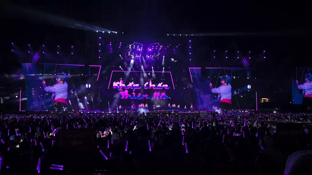 Sân khấu concert nhìn từ xa với màn LED giữa hiện chữ Khắp Chốn Thiên Hà màu hồng và biển lightstick tím khắp khán đài