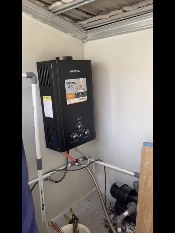 Water heater gas hitam dipasang pada dinding ruang separa terbuka bersama paip fleksibel keluli