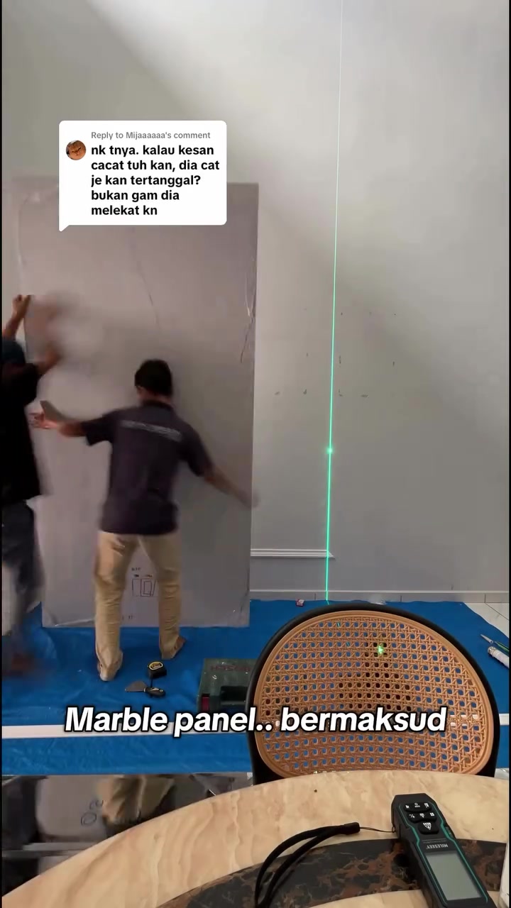 Dua pekerja memasang panel marmar besar di dinding dengan bantuan garisan laser
