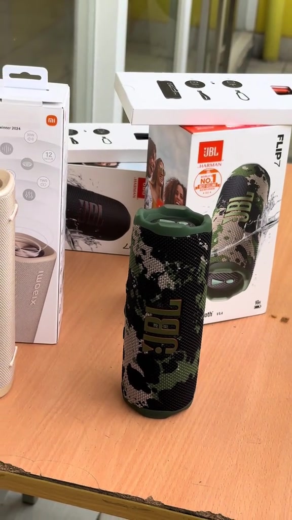 Loa JBL Flip 7 họa tiết rằn ri đứng trên bàn gỗ, cạnh hộp sản phẩm in hình JBL Flip 7
