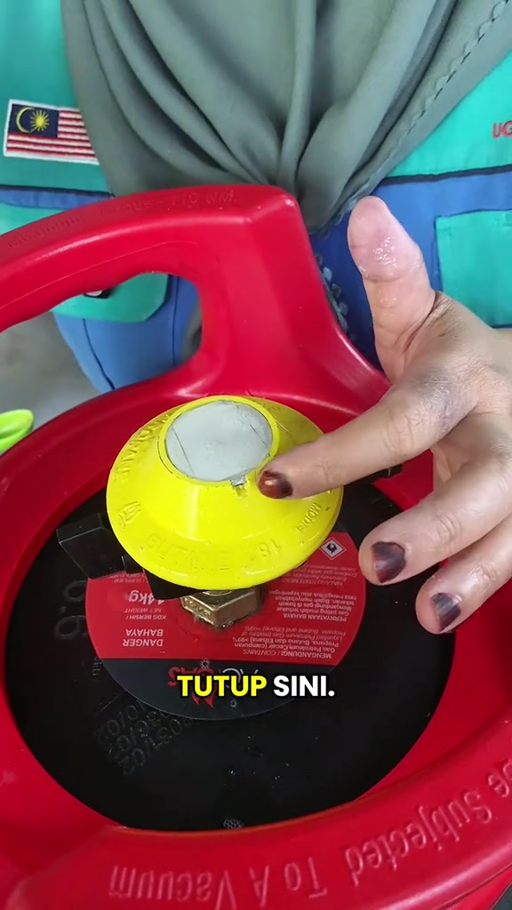 Tangan menunjuk kepala gas kuning di atas tong gas merah sebagai tempat tutup injap