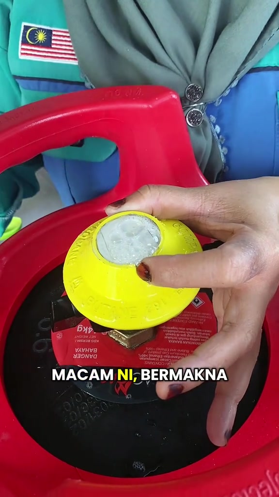 Tangan memegang kepala gas kuning di injap tong gas merah