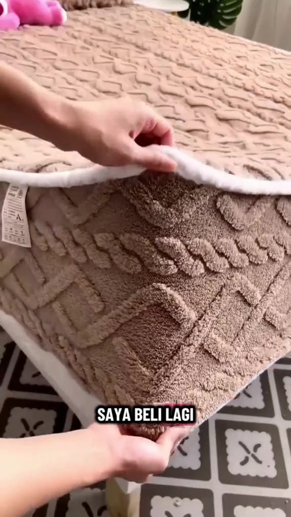 Tangan mengangkat penjuru cadar bulu braided warna kopi bergetah keliling sehingga nampak tag jagaan di penjuru tilam