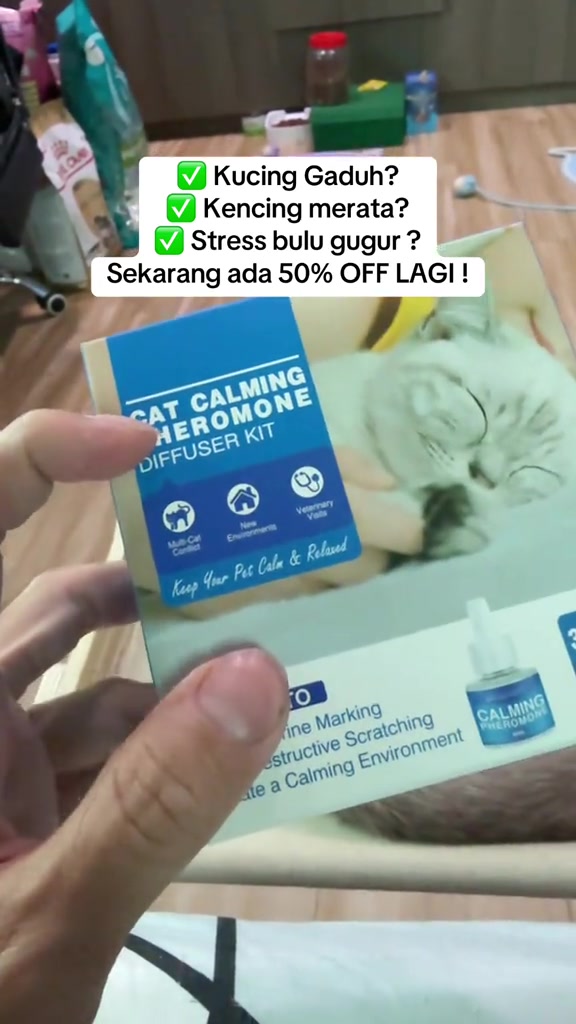 Kotak kit diffuser feromon penenang kucing dipegang di tangan, dengan gambar kucing tidur dan ikon kegunaan pada kotak