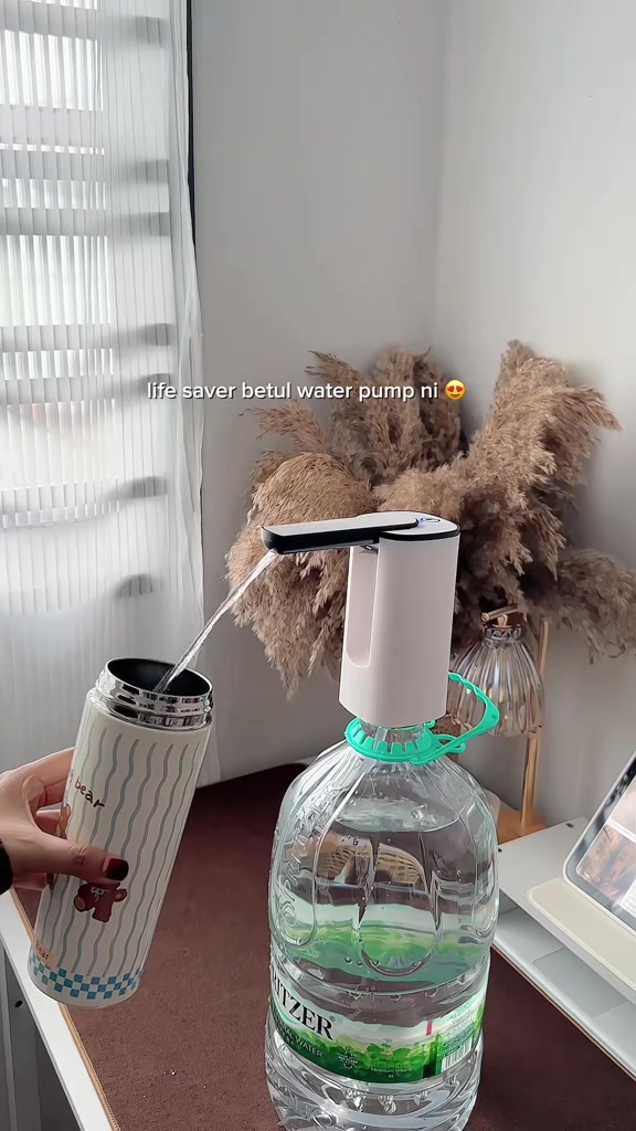 Pam botol elektrik putih menuang air ke dalam tumbler dari botol air besar