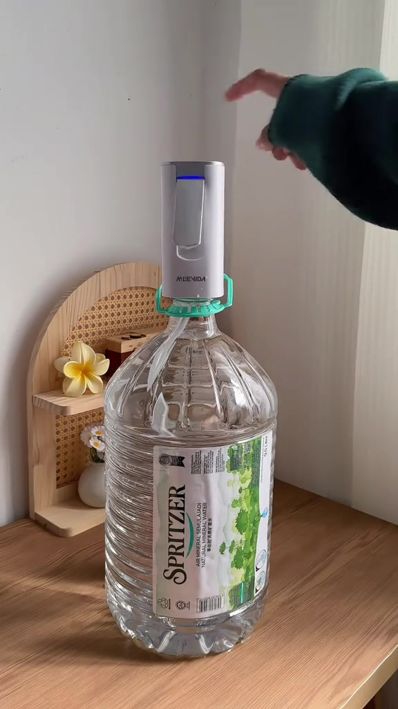 Pam botol elektrik dipasang pada mulut botol air besar di atas meja kayu