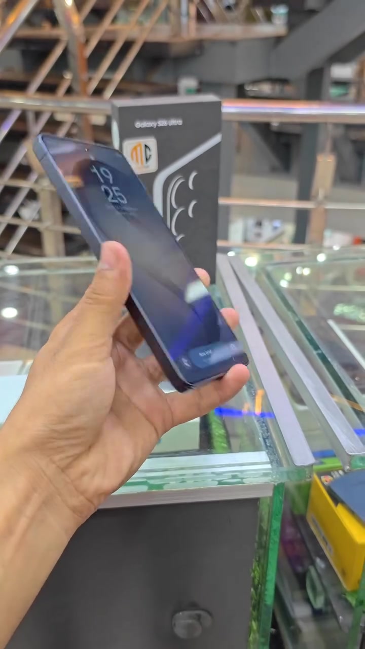 Unit Galaxy S26 Ultra dipegang di kaunter kedai dengan kotak asal berlabel di latar belakang