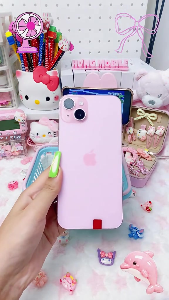 Mặt lưng iPhone 15 Plus màu hồng đặt giữa bàn trang trí nhiều phụ kiện