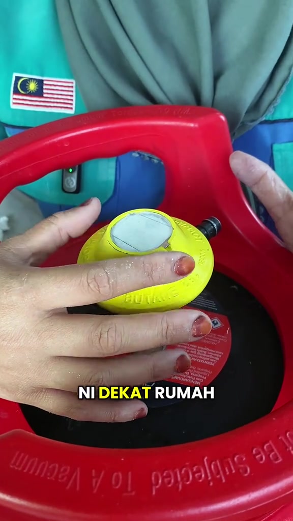 Dua tangan memeriksa kepala gas kuning di atas tong gas merah 14kg