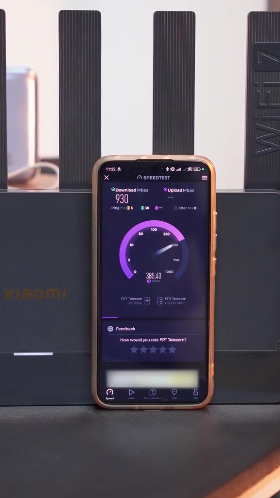 Điện thoại chạy Speedtest đạt 930 Mbps tải xuống và 388 Mbps tải lên, đặt trước router Xiaomi Wi-Fi 7 màu đen, server FPT Telecom