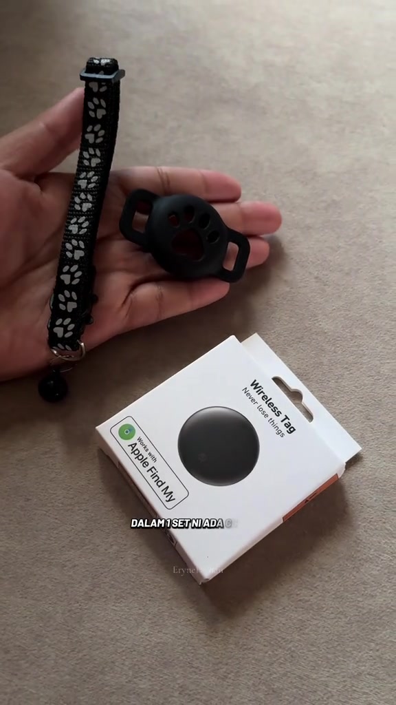 Tangan memegang holder silikon hitam bentuk tapak kaki dan collar kucing bert loceng, di sebelah kotak tag tanpa wayar serasi Apple Find My