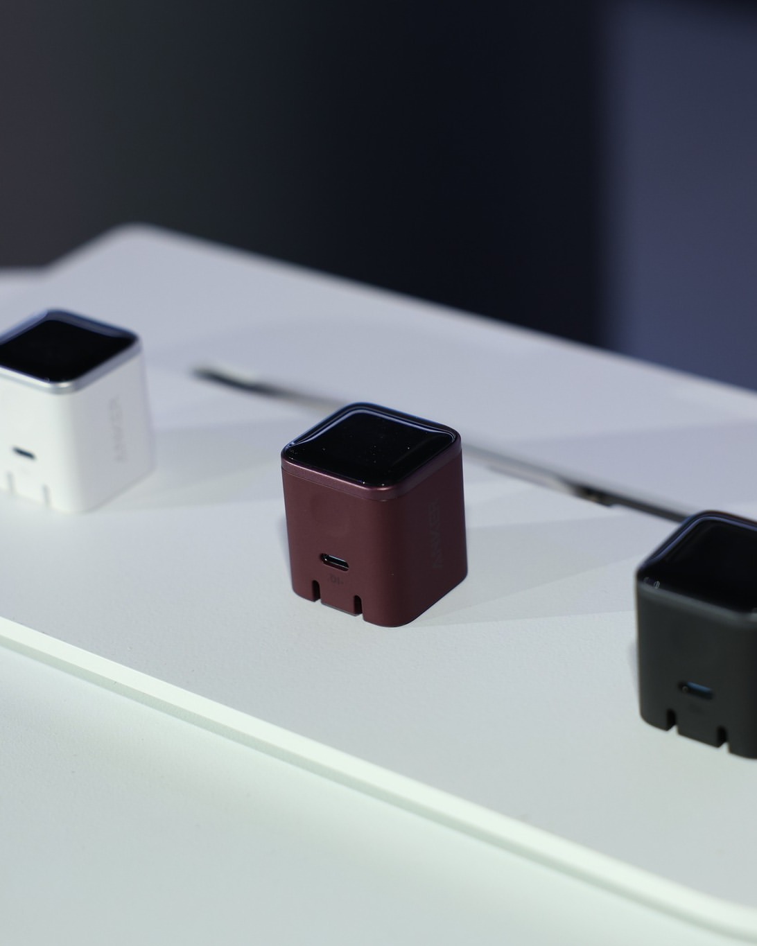 Tiga unit Anker Nano Charger 45W Smart Display warna putih, merah burgundy dan hitam dipamerkan atas rak putih