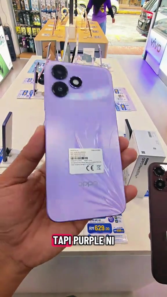 OPPO A6c warna ungu dipegang di kaunter kedai, dengan tag harga RM629.00 dan RM699.00 kelihatan di bawahnya