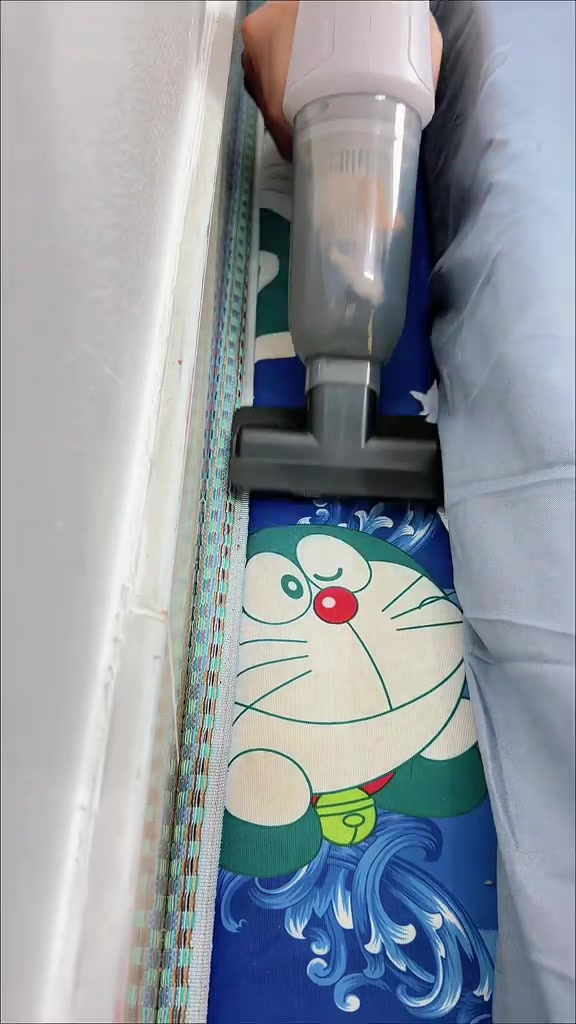 Máy hút bụi cầm tay gắn đầu bản rộng đang hút khe mép nệm họa tiết Doraemon