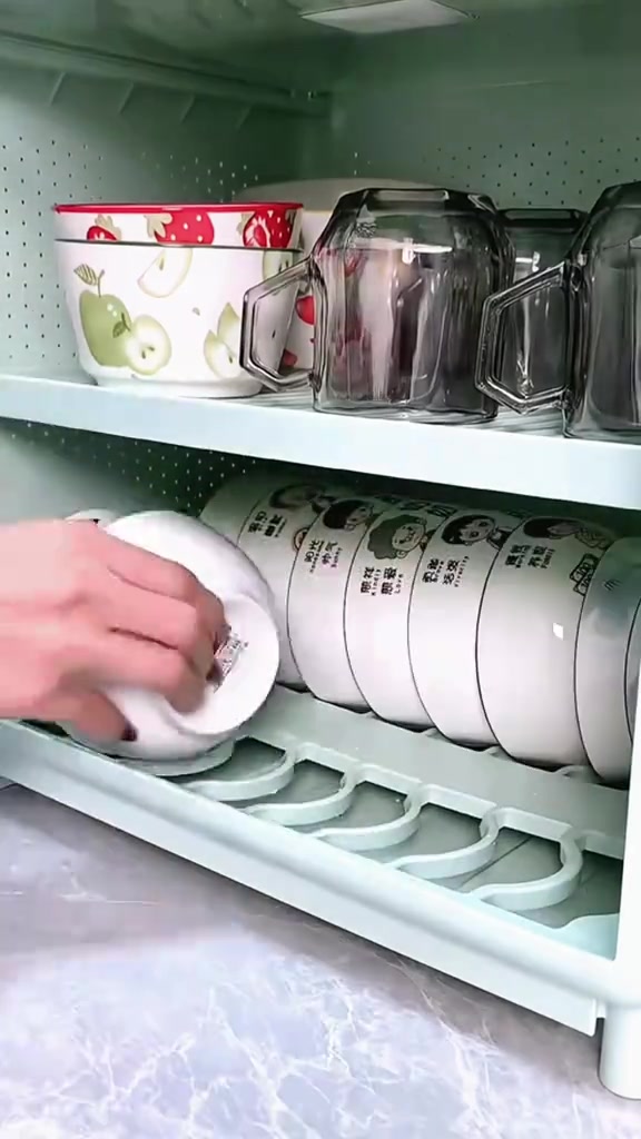Tangan menyusun mangkuk ke dalam rak pinggan bertingkat bertutup di dapur