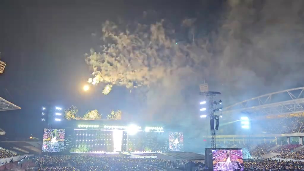 Sân khấu concert BIGBANG tại sân Mỹ Đình nhìn từ khán đài cao, hai màn hình lớn chiếu đồ họa sáng, dưới sân là biển đèn lightstick của khán giả