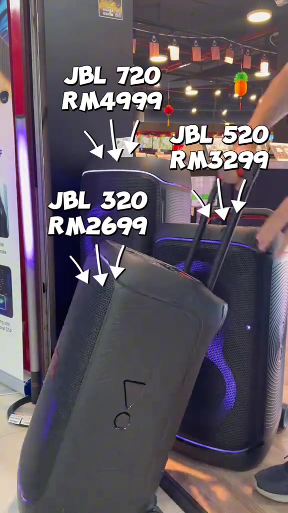Deretan speaker JBL PartyBox dalam kedai fizikal dengan label harga JBL 720 RM4,999, JBL 520 RM3,299 dan JBL 320 RM2,699 serta tangan pelanggan pada pemegang