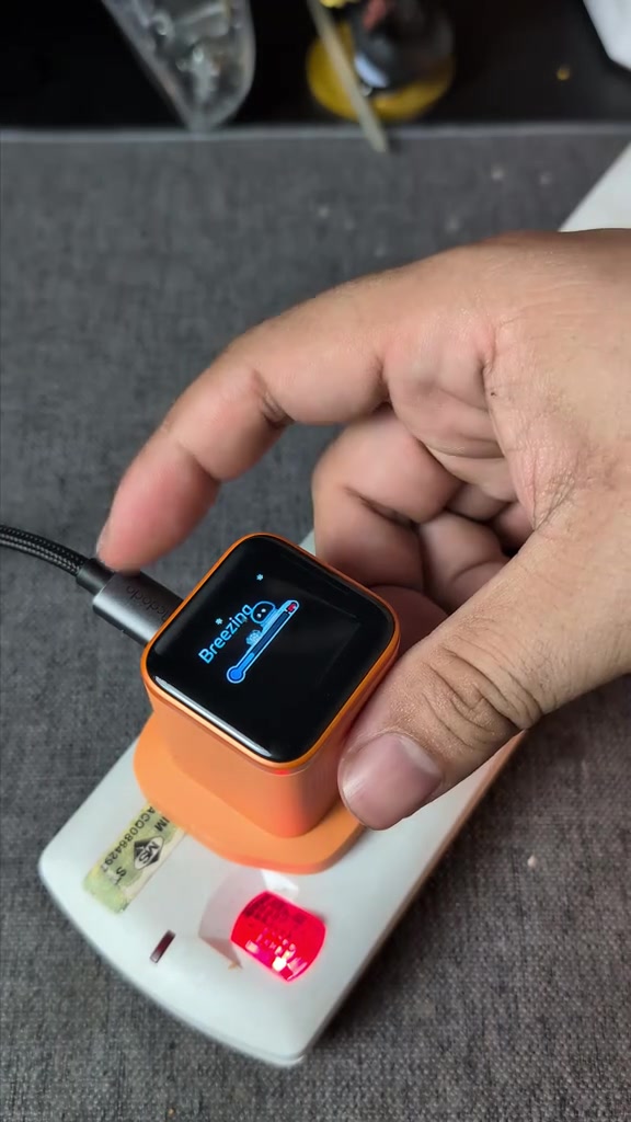 Pengecas Anker Nano berwarna jingga dicas pada extension socket putih di Malaysia, skrin pintar menunjukkan animasi Breezing beserta bar bateri