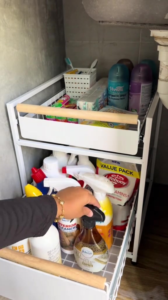 Rak drawer putih bawah sinki berisi botol spray pencuci dan sabun, tangan sedang menarik drawer keluar