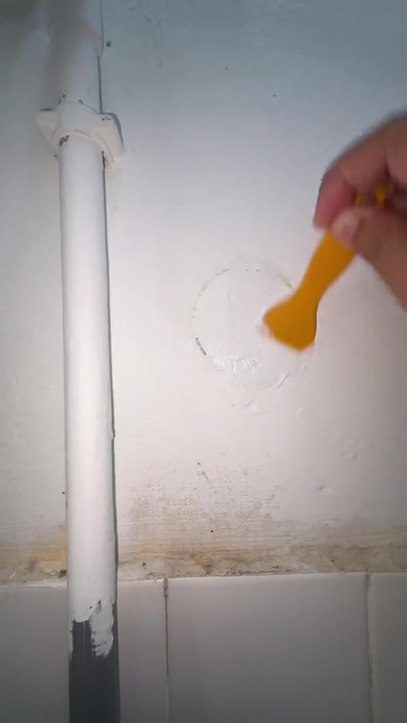 Spatula oren meratakan paste putih pada kesan bulatan bekas tampalan di dinding