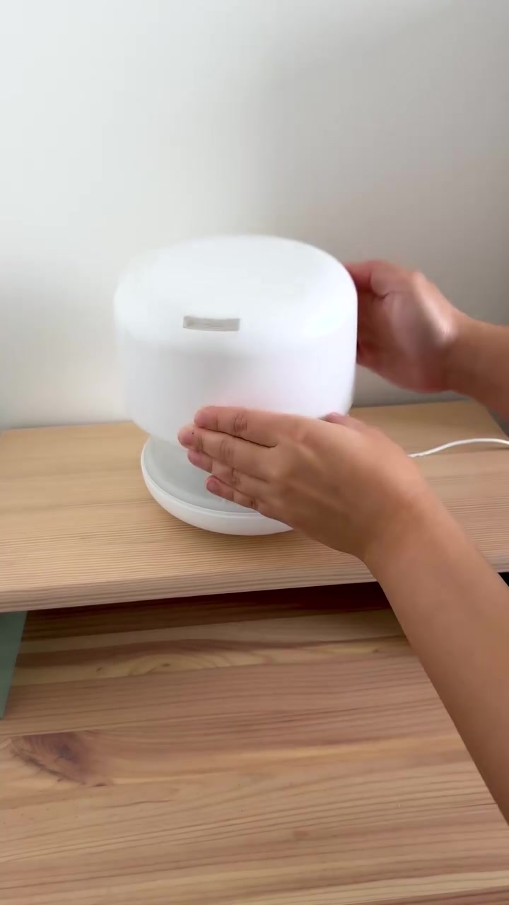 Tangan memasang penutup diffuser ultrasonik putih bulat di atas rak kayu