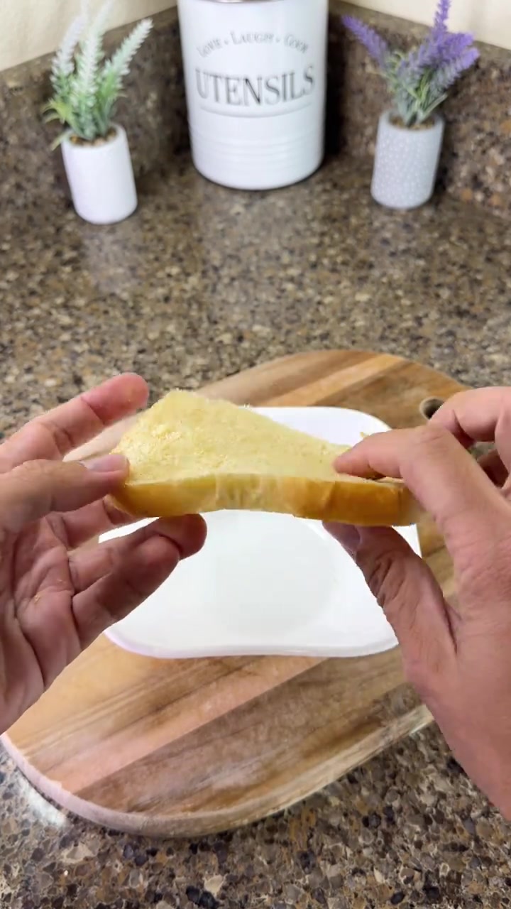 Dua tangan memegang sekeping roti sebagai umpan perangkap tikus di atas pinggan dan papan kayu