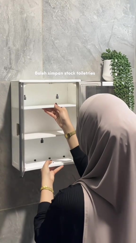 Pandangan belakang wanita bertudung menyusun papan rak dalam kabinet dinding putih