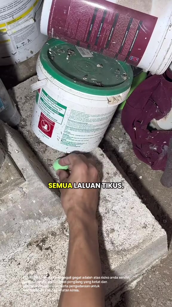 Tangan meletakkan biji bulat hijau penghalau tikus di tepi baldi simen dalam stor