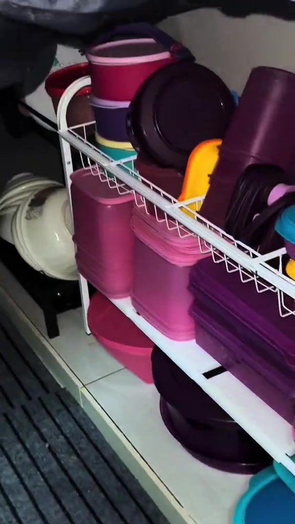 Rak wayar putih di bawah sinki berisi bekas plastik bertutup warna merah jambu dan ungu serta mangkuk tersusun