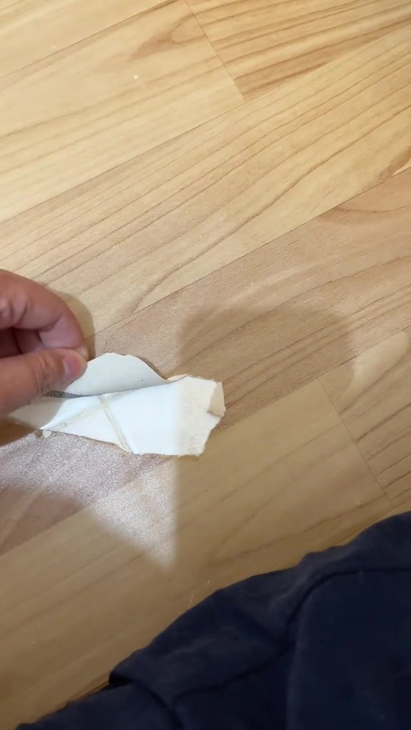 Tangan memegang sekeping plastik putih yang sudah dikunyah kucing di atas lantai kayu