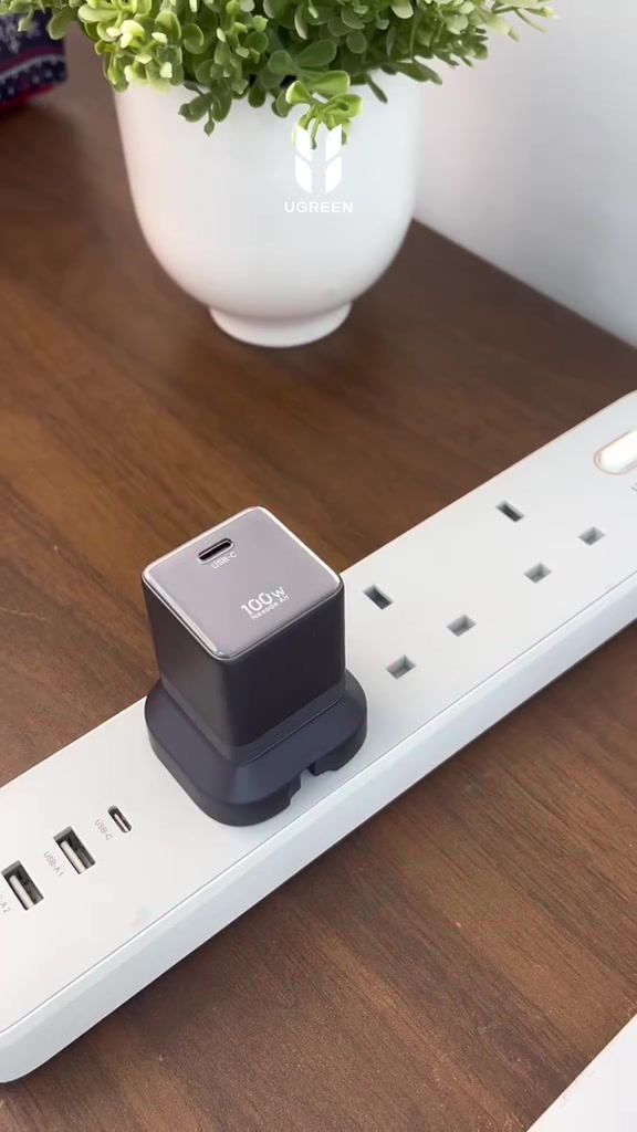 Pengecas UGREEN Nexode Air 100W warna kelabu gelap tercucuk pada extension socket putih, dengan tulisan 100W pada muka atasnya