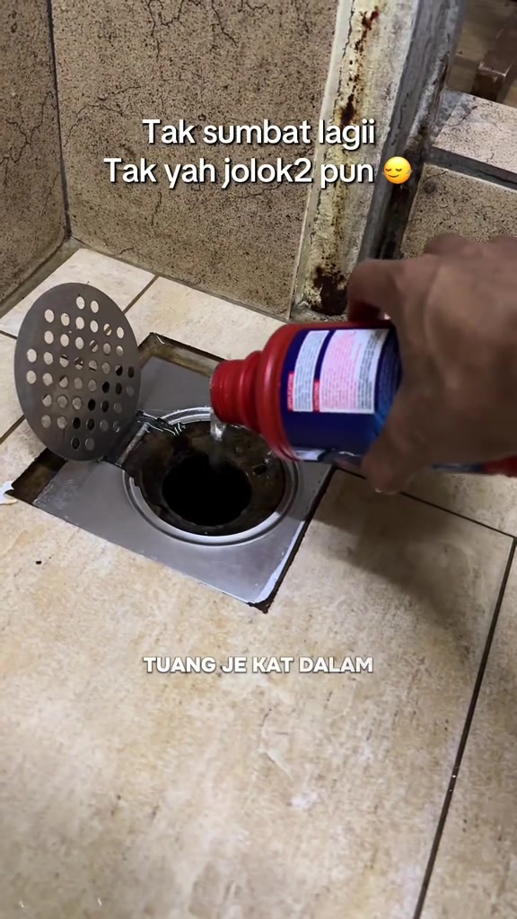 Tangan menuang cecair clog remover dari botol merah biru ke dalam perangkap lantai