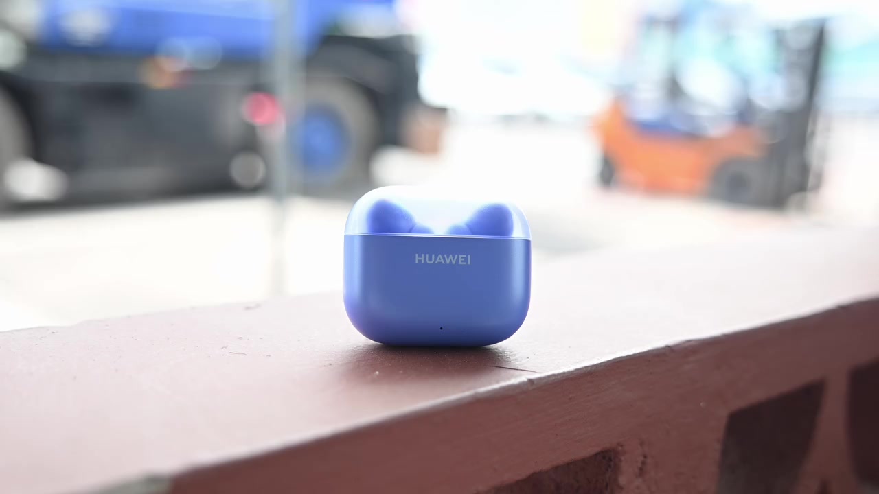 Bekas pengecas biru HUAWEI FreeBuds SE 5 MAX diletakkan atas birai dengan latar jalan raya kabur