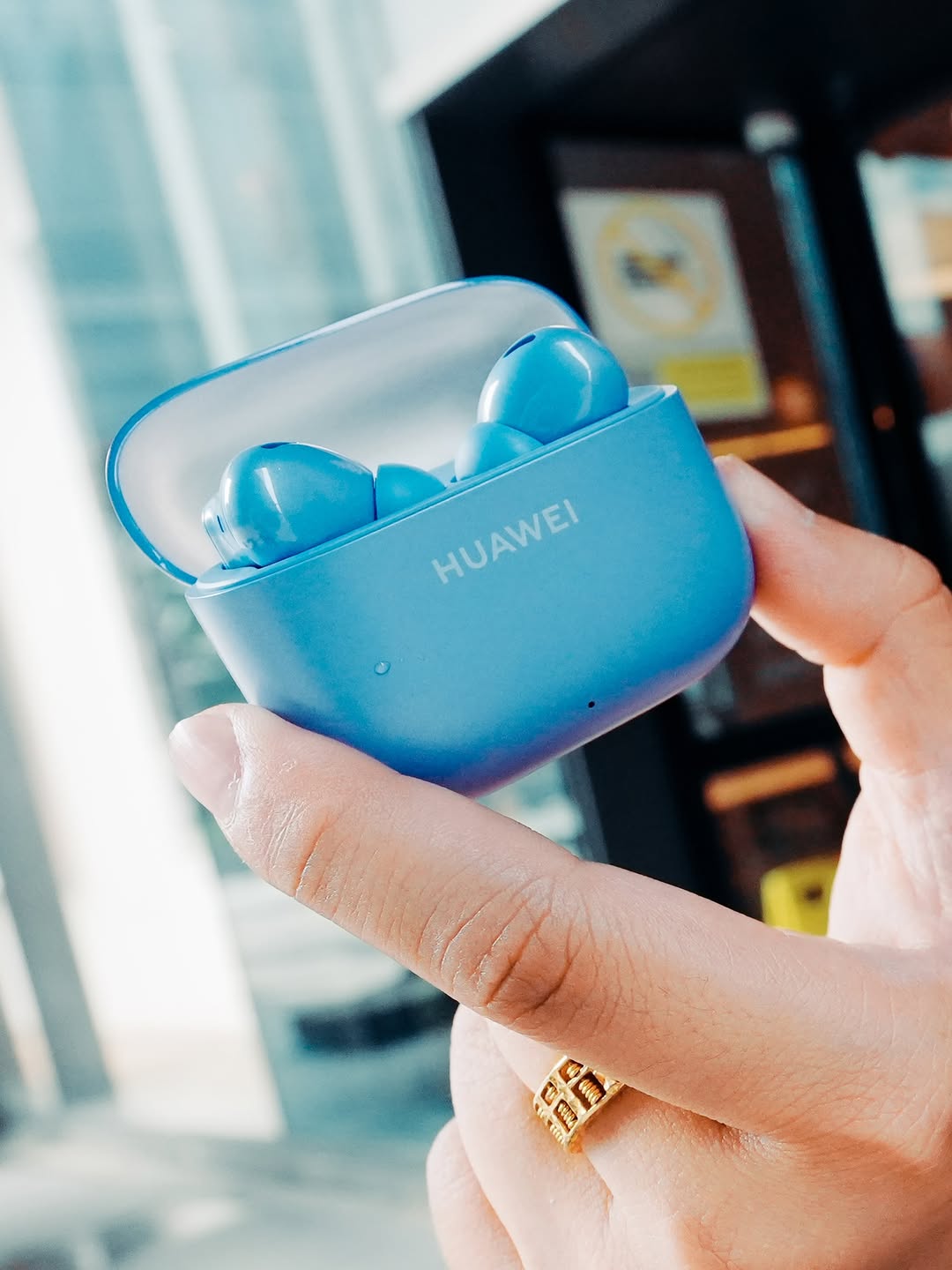 Bekas pengecas biru HUAWEI FreeBuds SE 5 MAX dengan penutup separa lutsinar terbuka dipegang pada tangan