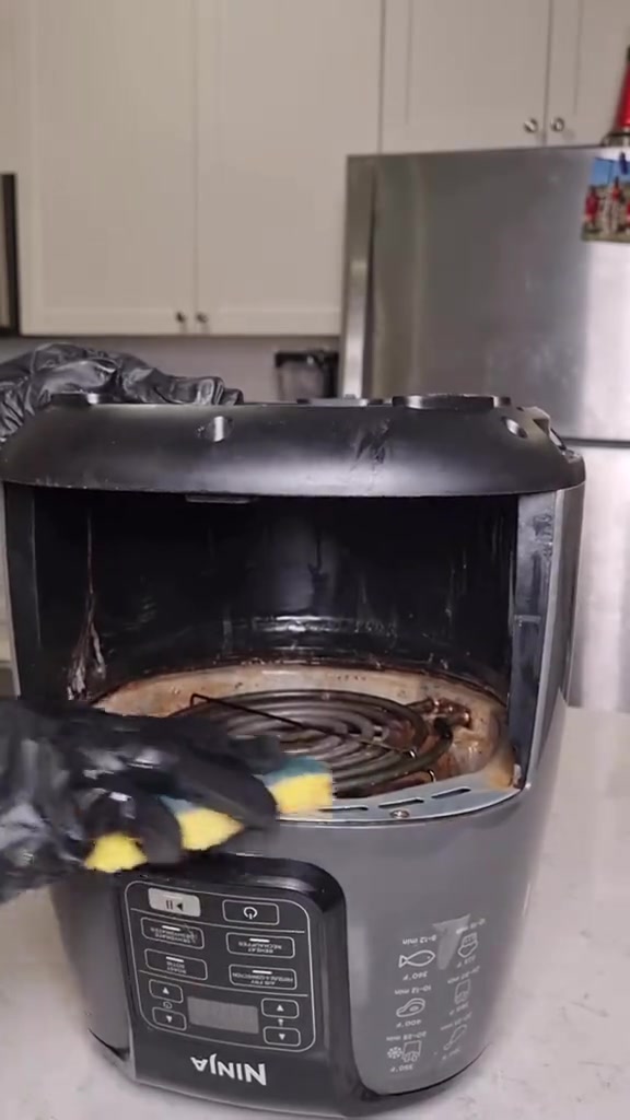 Tangan bersarung hitam mengelap bahagian elemen pemanas air fryer dengan span lembut kuning
