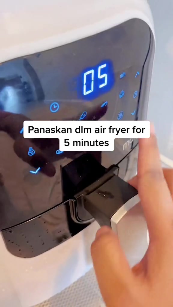 Jari menekan panel sentuh air fryer yang ditetapkan 5 minit untuk memanaskan dan melonggarkan kerak
