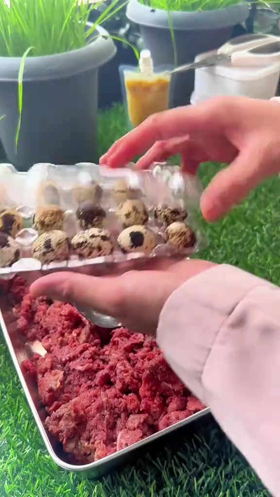Tangan memegang tray telur puyuh di atas tray daging mentah yang telah dikisar
