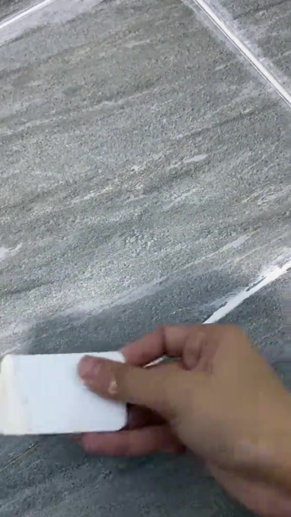 Tangan melicinkan grout putih di celah jubin lantai kelabu guna kepingan plastik putih