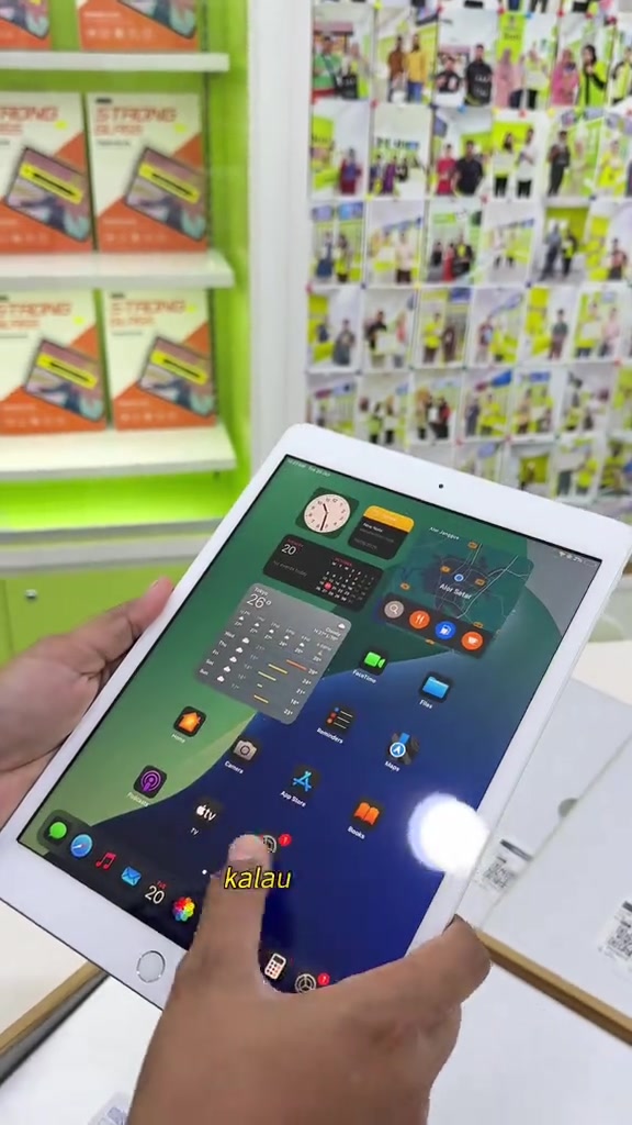 Tangan memegang iPad putih paparan skrin utama dengan widget di dalam store 3cat, rak aksesori di latar belakang