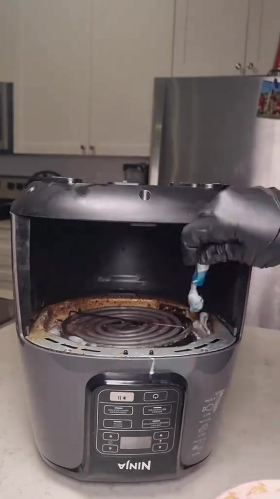 Tangan bersarung hitam menyapu pes baking soda pada elemen pemanas air fryer guna berus gigi