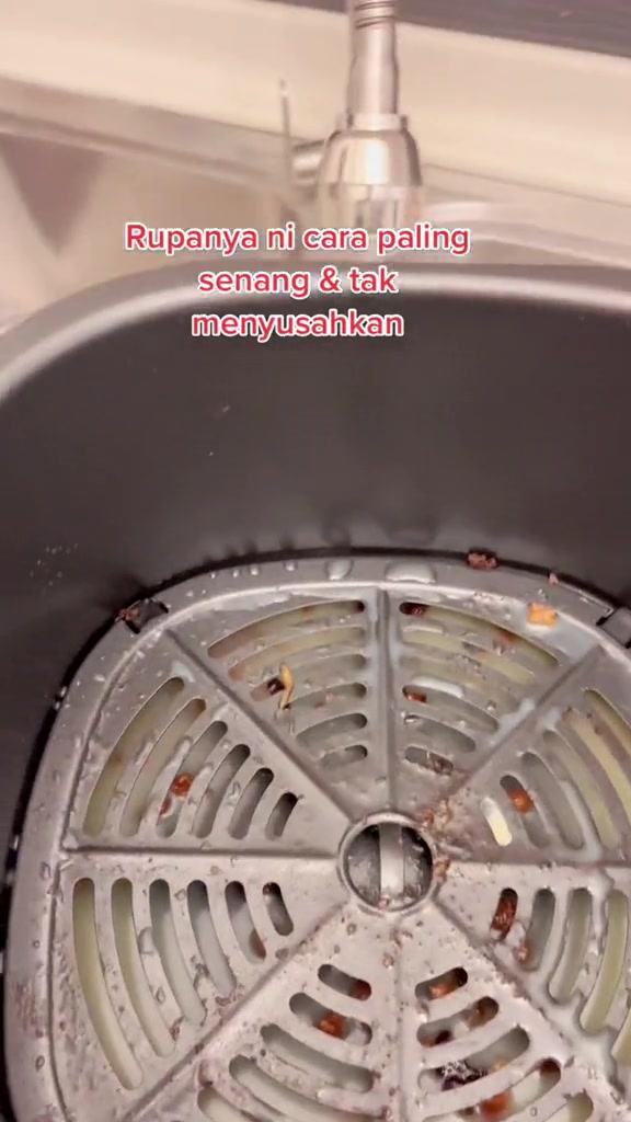 Gril basket air fryer dengan sisa makanan terlekat di celah-celah, diletakkan di sinki bawah paip