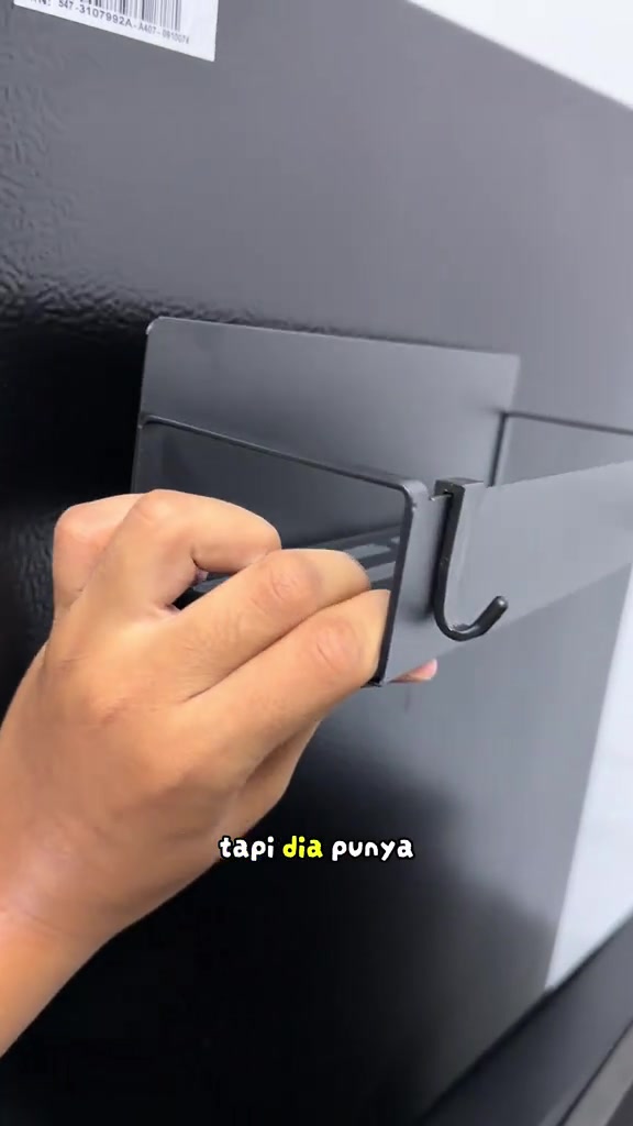 Tangan memegang rak magnet bercangkuk yang sudah dipasang pada peti sejuk.