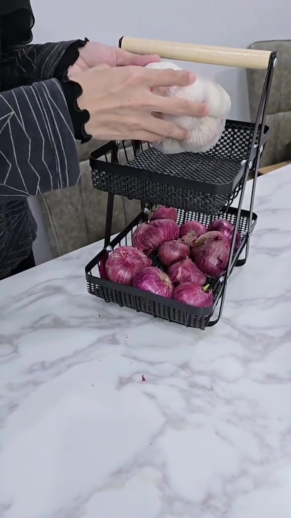 Tangan meletakkan bawang putih dalam bakul berlubang dengan bawang merah disimpan di tingkat lain