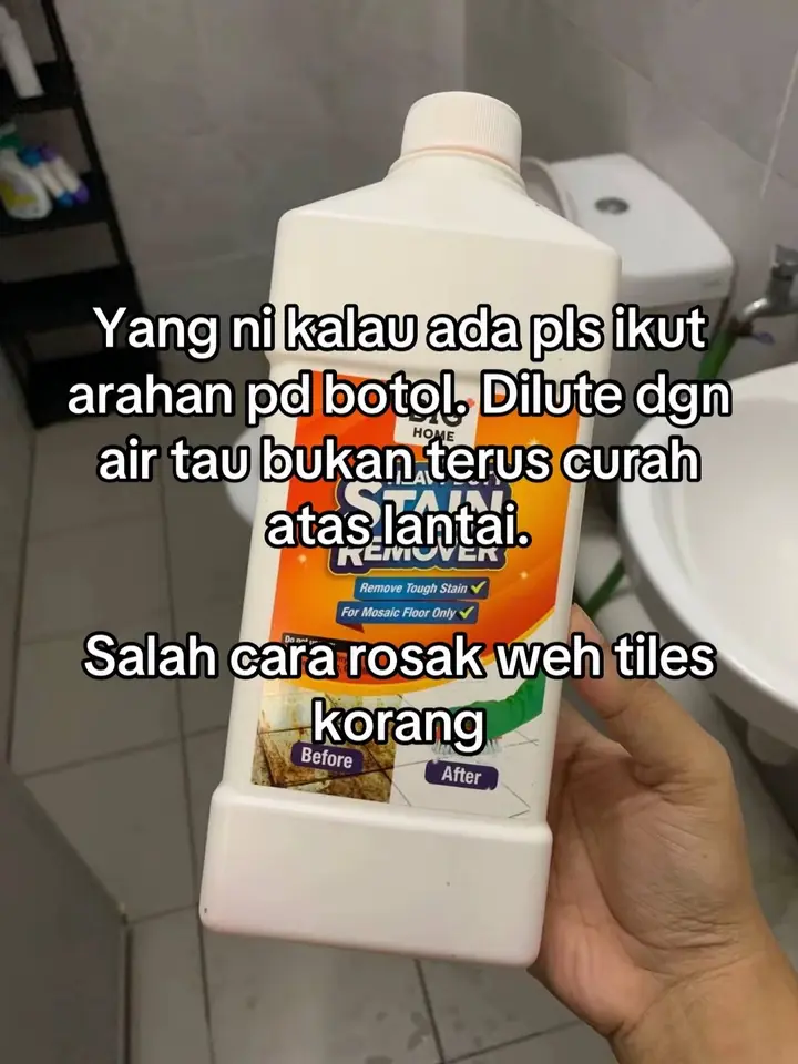 Tangan memegang botol pencuci lantai putih di hadapan sinki dan dinding jubin