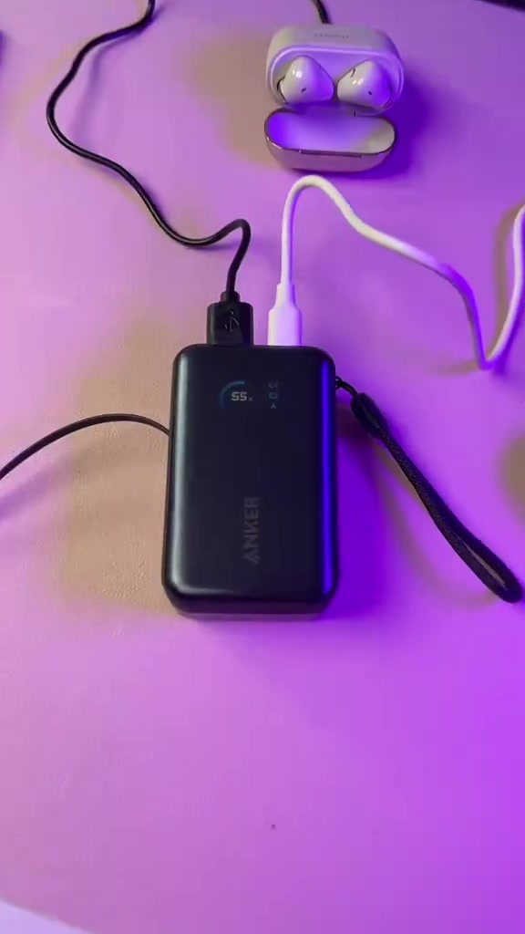 Power bank Anker dengan paparan digital di tengah kabel dan aksesori pengecasan pada latar ungu.