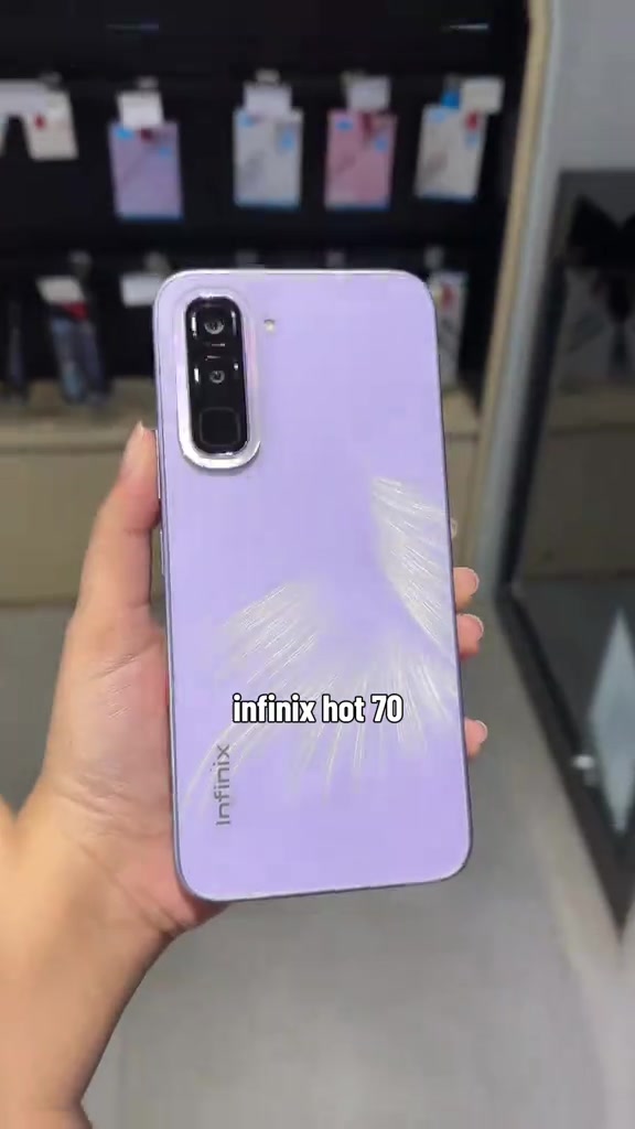 Telefon HOT 70 ungu muda dipegang dari belakang, dengan modul kamera jelas kelihatan