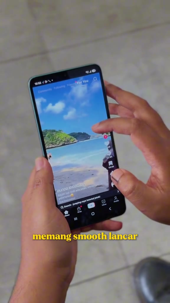 Telefon Galaxy A08 dipegang dengan dua tangan, skrin memaparkan suapan video