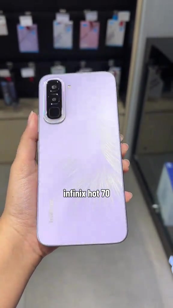 Bahagian belakang Infinix HOT 70 berwarna ungu muda yang dipegang dengan tangan