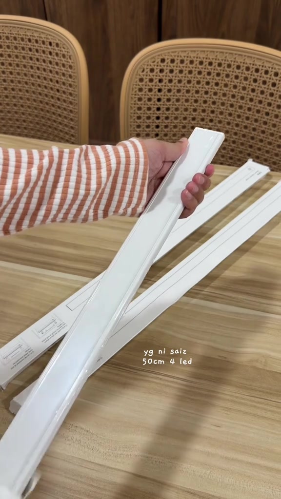 Tangan memegang bar lampu putih memanjang dengan beberapa bar lain di atas meja