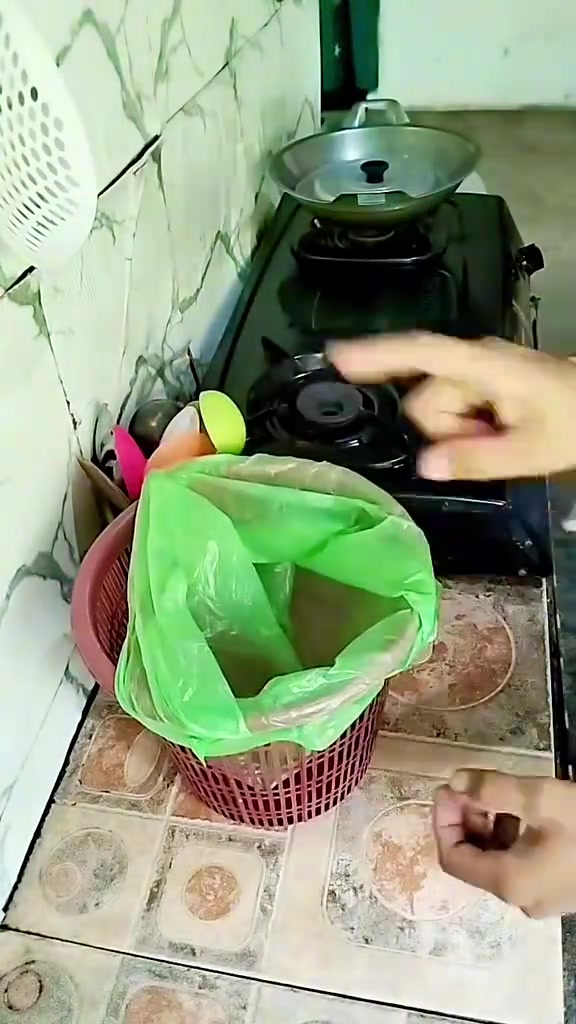 Tangan memasang beg plastik hijau pada bakul kecil di dapur